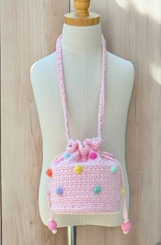 a pink crocheted purse with pom - poms hanging from the front