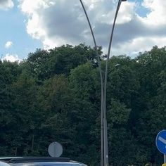 two cars are stopped at an intersection with trees in the background and one car is driving down the street