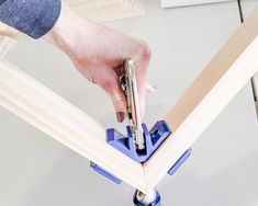 a person holding a piece of wood on top of a table with a pair of scissors