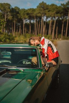 a woman leaning on the hood of a green car with trees in the back ground