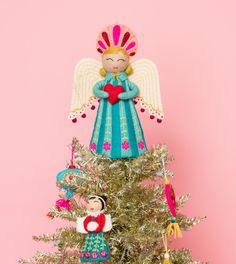 an angel figurine sitting on top of a christmas tree next to a pink wall