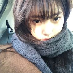 a woman with long brown hair wearing a scarf and looking at the camera while sitting in a car