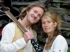 a man holding a guitar next to a woman with long blonde hair and white shirt