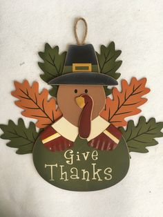 a wooden ornament with a turkey wearing a pilgrim hat and leaves on it