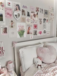 a white bed topped with lots of pink and white pillows next to a wall covered in pictures