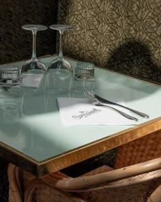 a table with two wine glasses and silverware on it, next to a basket