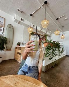 a woman sitting at a table with a drink in her hand and plants hanging from the ceiling