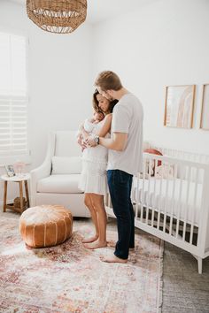 a man and woman standing in front of a white crib with a baby on it