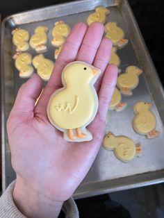 a hand holding a cookie shaped like a duck and some cookies on a baking sheet