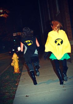 two people dressed up as batman and robinette running down the street at night time