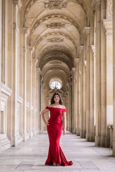 a woman in a red dress is posing for the camera while standing on an archway way