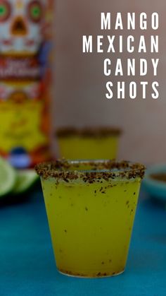 a cup filled with yellow liquid sitting on top of a blue table next to a can of mexican candy shots