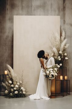 a bride and groom kissing in front of a backdrop with flowers, candles and pamonini