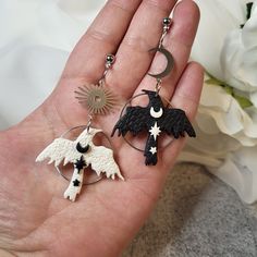 the hand is holding two earrings that are decorated with black and white sheeps, sun and moon