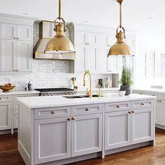 an instagramted photo of a kitchen with white cabinets and gold pendant lights over the island