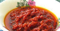 a white bowl filled with red sauce on top of a floral tablecloth covered table