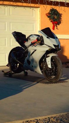 a white motorcycle parked in front of a garage with a wreath on the wall behind it