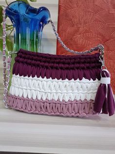 a purple and white purse sitting on top of a table next to a blue vase