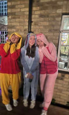 three people in costumes standing next to each other near a brick building at night time