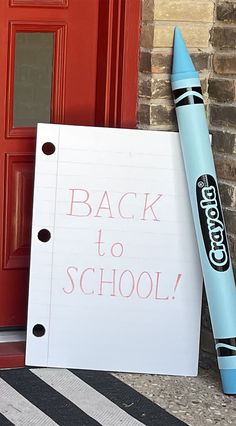 a back to school sign next to a red door with a blue crayon pen