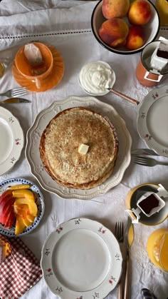 a table topped with plates and bowls filled with food next to oranges, peaches and whipped cream