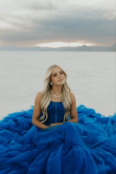 a woman in a blue dress sitting on the beach