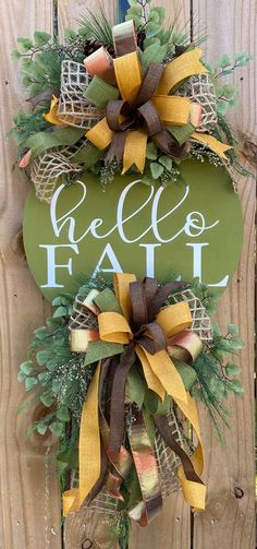 a green sign that says hello fall hanging on a wooden fence with yellow and brown bows