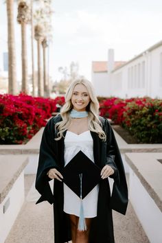 a woman wearing a graduation gown and holding a black and white graduate's cap