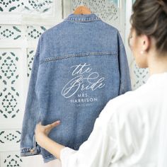 a woman standing in front of a mirror wearing a jean jacket with the bride's name on it