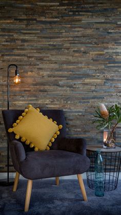 a chair with a yellow pillow on it in front of a wall that is made out of wood planks