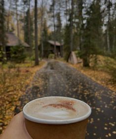 a person holding up a cup of coffee in the middle of a road with trees and houses on both sides