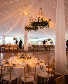 the inside of a tent with tables, chairs and chandeliers set up for an event