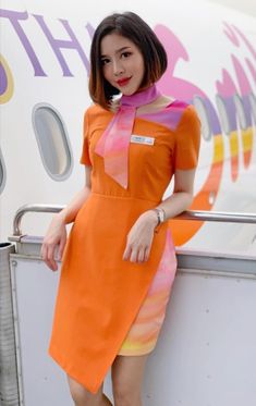 a woman in an orange and pink dress leaning against the side of an airplane door