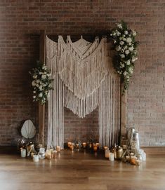 a wedding ceremony setup with macrami, flowers and candles on the floor in front of a brick wall