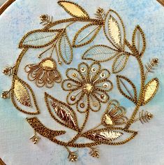 an embroidery project with gold thread and flowers on blue fabric, in the shape of a circle