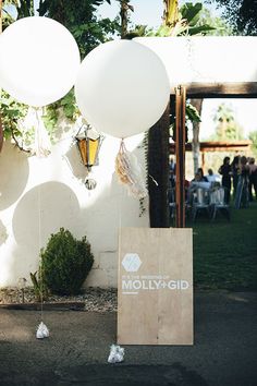 white balloons are tied to a wooden sign