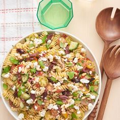 a bowl filled with pasta salad next to wooden spoons and utensils on a table