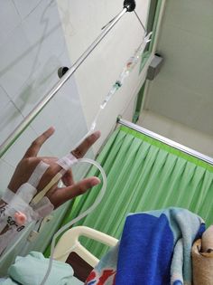 someone is holding their hand up to an iv in a hospital room with green curtains