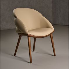 a beige leather chair with wooden legs on a gray floor in front of a concrete wall