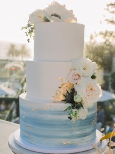 a white and blue wedding cake with flowers on top