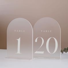 two clear acrylic table numbers sitting next to each other on a white surface