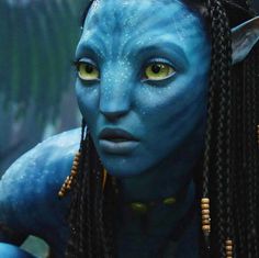 a woman with blue makeup and braids looks at the camera while wearing yellow eyes