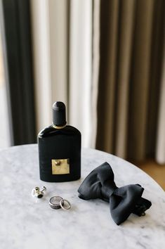 two rings and a bottle sitting on a table next to a pair of black bow ties