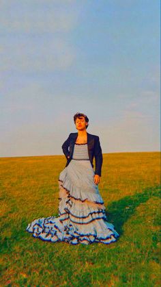 a woman in a dress standing on top of a grass covered field next to a blue sky