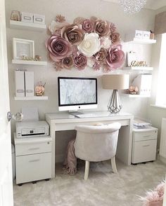 a desk with a computer on top of it next to a lamp and some flowers