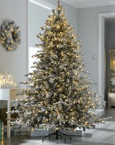 a white christmas tree in a living room with snow on the ground and lights around it