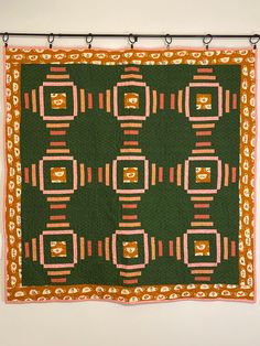 a green and orange quilt hanging on a wall