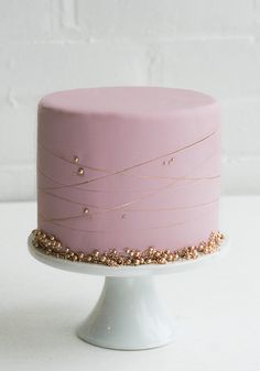 a pink cake with gold sprinkles on top sitting on a white pedestal