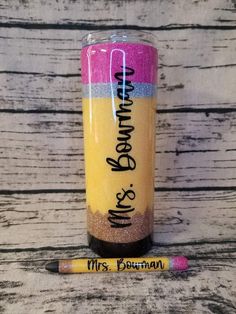 a yellow and pink tumbler next to a pencil on a wooden table with writing