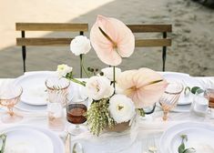 the table is set with white plates, silverware and pink flowers in vases